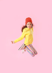 Adorable little girl in yellow hoodie jumping on pink background
