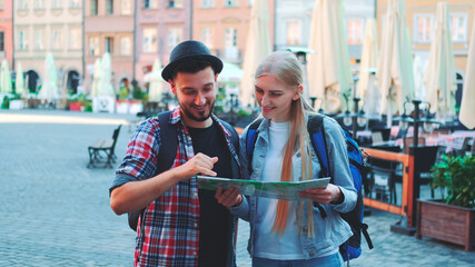 Fototapeta premium Zoom shot of tourists holding map and smiling to the camera. They standing on a big market square of old european city.