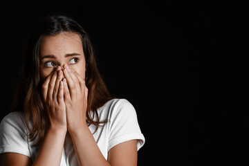 Scared young woman on black background. Violence concept