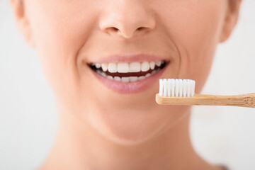 Woman with bamboo tooth brush on light background, closeup