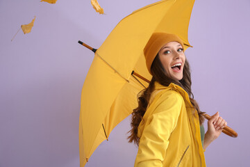 Happy woman in raincoat with opened umbrella on color background