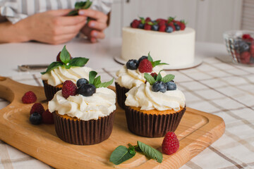 Women's hands decorate muffins with fresh blueberries and raspberries and mint leaves. English