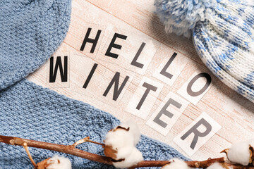 Composition with text HELLO WINTER, warm hat, sweater and cotton branch on light wooden background, closeup