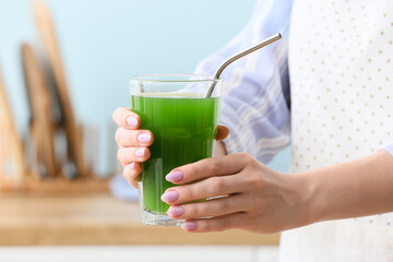 Woman with glass of green juice in kitchen, closeup