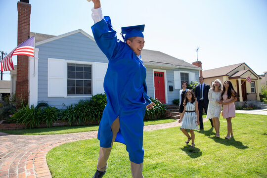 Exuberant graduate holding diploma with family front yard