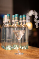 A cold martini is served in a cocktail glass and presented in front of several generic unlabelled bottles.