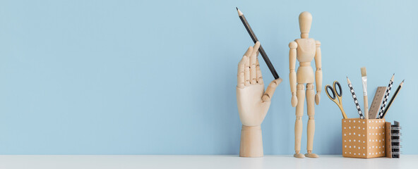 Table with desk objects, office supplies, books, and plant on a pastel blue background.	