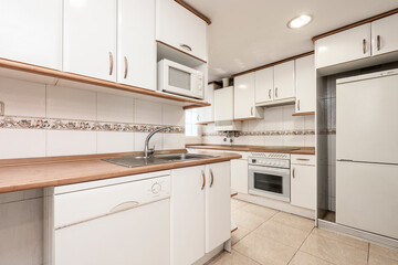 Kitchen with white cabinets and appliances, wooden worktop and stainless steel sink