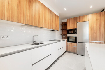 Fototapeta na wymiar Nice newly installed kitchen with wood grain cabinets combined with white cabinets and stainless steel appliances