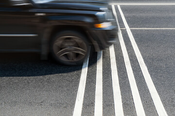 Rumble strips or speed breakers  on asphalt road surface and black car crossing them in motion blur. Traffic calming concept.
