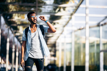 Fototapeta premium Black man with glasses and backpack walking down the street