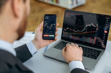 Close-up of a laptop and cellphone screen with stock diagrams. Crypto trader investor broker using...