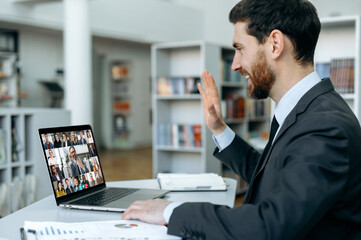 Fototapeta na wymiar Online video communication. Side view of business person communicating by video conference with group of business partners of different nationalities, using laptop while sitting in modern office
