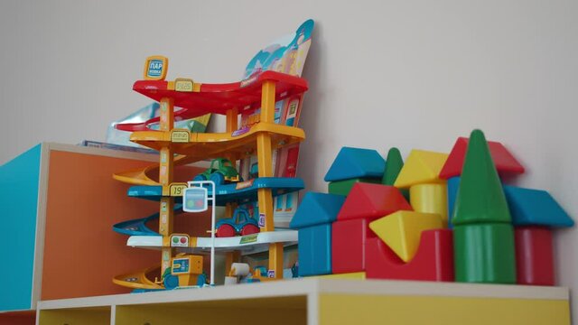 Colorful plastic toy parking area and constructor set blocks on cabinet in light playroom of kindergarten close view