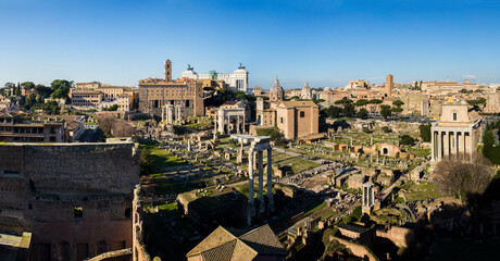 Wide panoramic view of the Roman Forum from the Palatine hill in Rome, Italy. Ruins of the ancient Roman temples. Marble columns under the blue sky. Medieval and Rainessance churches