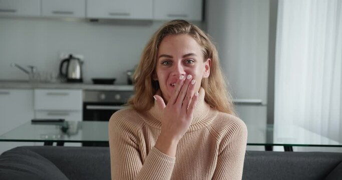Front view. Attractive blonde girl says wow in surprise while looking at the camera and covers her mouth with her hand