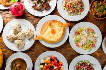 Georgian cuisine foodset from khachapuri, khinkali, pkhali, dolma, satsivi , ajara khachapuri, salad caesar with chicken, fried khinkali, top view on wooden table