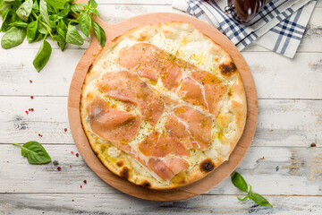 Pizza with prosciutto, cheese and oregano on wooden board top view on white wooden table