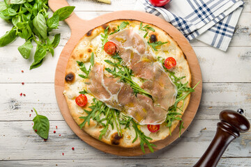 Pizza with Parma ham and arugula and tomatoes on the board top view on white wooden table, primavera