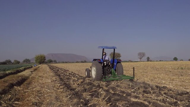 Full shot of a real farmer plowing the field with his tractor, preparing the soil to plant new seeds