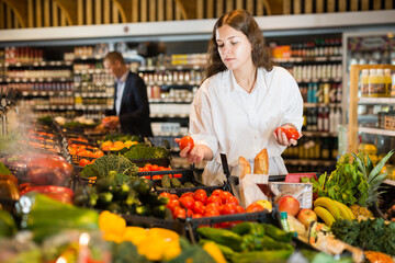 Female shopper picks ripe tomatoes on grocery store shelves