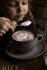 Five-year-old girl drinks cocoa in cafe. European coffee shop.
