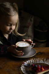 Five-year-old girl drinks cocoa in cafe. European coffee shop.