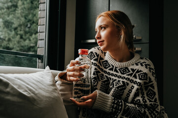woman drinking water looking out the window at home