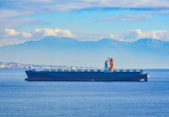 Big cargo ship in the Gulf of Naples, city coastline, mountains and blue sky with clouds