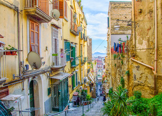 Fototapeta na wymiar Typical street of Naples old town: narrow, steep, delapidated, picturesque, with jalousies on windows, flower pots and drying laundry