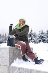 Vertical portrait of beautiful attractive happy positive cheerful girl young black African Afro American woman is having fun smiling walking in winter snowy park at snow frosty day in hat and gloves