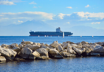 Stone pier, big cargo ship and many small optimist-class sailboats in the Gulf of Naples