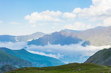 Fototapeta na wymiar Caucasian mountains in Kazbegi national park in Georgia, blue sky with clouds, rocks, stones, fog in canyons, green grass