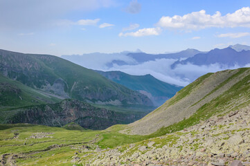 Fototapeta na wymiar Caucasian mountains in Kazbegi national park in Georgia, blue sky with clouds, rocks, stones, fog in canyons, green grass