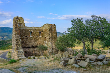 Fototapeta na wymiar Fortress tower of Jvari Monastery - clifftop orthodox monastery dating to circa 590 CE, in Georgia. Blue sky with clouds, ancient stone walls, dry yellow grass, gren trees, mountains on the background