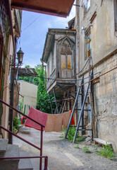 Fototapeta na wymiar Traditional georgian house in Tbilisi yard. Stone walls, wooden balcony, drying laundry, green trees and grass, blue sky, old lantern