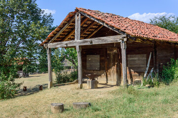 Traditional georgian house in Tbilisi open-air ethnographical museum. Wooden walls, tiled roof, dry grass, green trees and bushes, blue sky