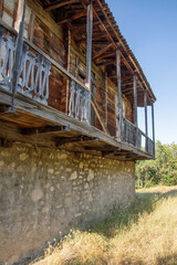 Abandoned traditional georgian house in Tbilisi. Stone and wooden walls,  ruined wooden balcony, dry grass, green trees, blue sky