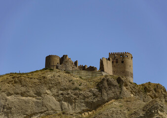Fototapeta na wymiar Ksani fortress, also known as the Mtkvari fortress in eastern Georgia, perched on a mount at the confluence of Ksani and Kura rivers. Brown brick and stone ancient walls, blue sky, stone cliff