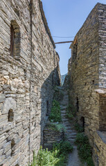 Narrow village street in the Fortified Village of Shatili, Khevsureti, Georgia. Abandoned houses, grey old stone walls, green bushes and grass, stone stairs, blue sky with clouds.