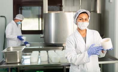 Woman in protective mask showing cottage cheese production process on dairy factory