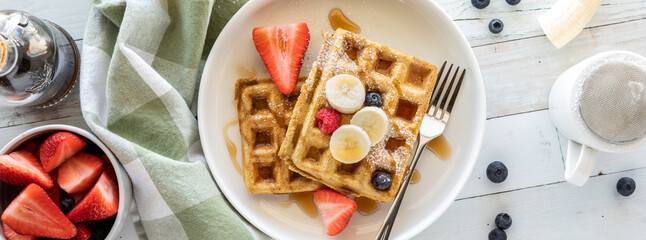 Top down view of whole grain waffles topped with fresh fruit and powdered sugar.