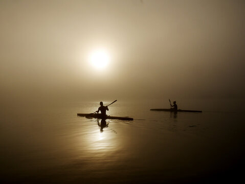 Two kayakers training on a still, foggy morning. 