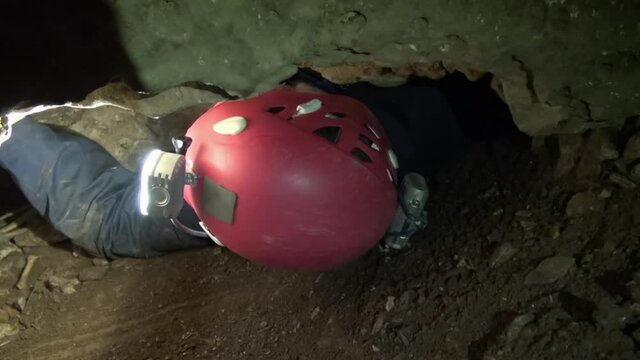 Male caver squeezes through tight rock restriction in underground cave