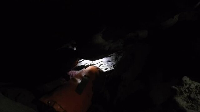 Deep inside small cave passage, female spelunker hands off gear bag