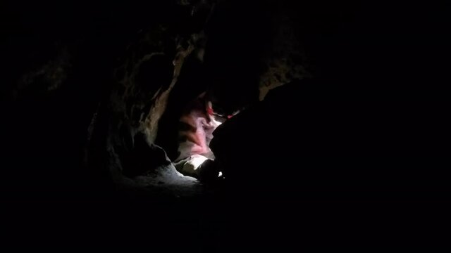 Expedition caver drags gear bag down dark narrow passage in blackness