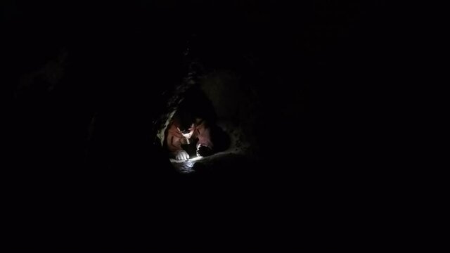 Female expedition caver crawls through tight dark cave passage