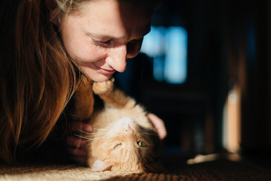 young woman playing with ginger cat