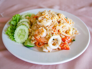 Delicious Fried rice with seafood, egg, garlic, cucumber, lemon. Thai food called Khao pad thale. Shrimp, squid, octopus, crab Fried Rice on white ceramic plate. Selective focus