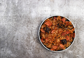 Bigos - traditional polish dish of stewed sauerkraut with prunes and sausages on a round plate on a dark gray background. Top view, flat lay